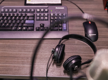 A digital workstation with recording equipment around it An unfocused microphone in the foreground with a keyboard and a pair of headphones on a desk in the back