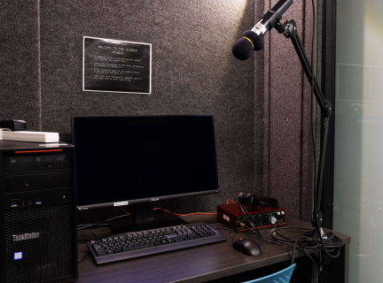 Photograph shows interior of recording studio, with computer, monitor and microphone featured prominently.