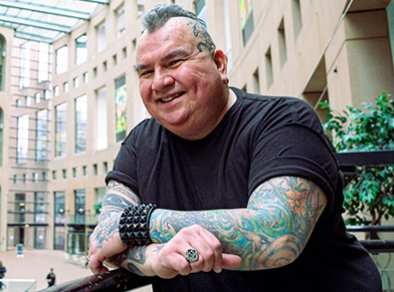 A man smiles and leans with his arms crossed on a balcony railing that overlooks the atrium of Vancouver Public Library's Central Library.