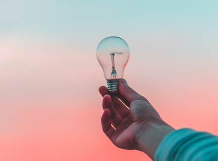 Need More Help image A hand holding a lightbulb against a pink sky backdrop