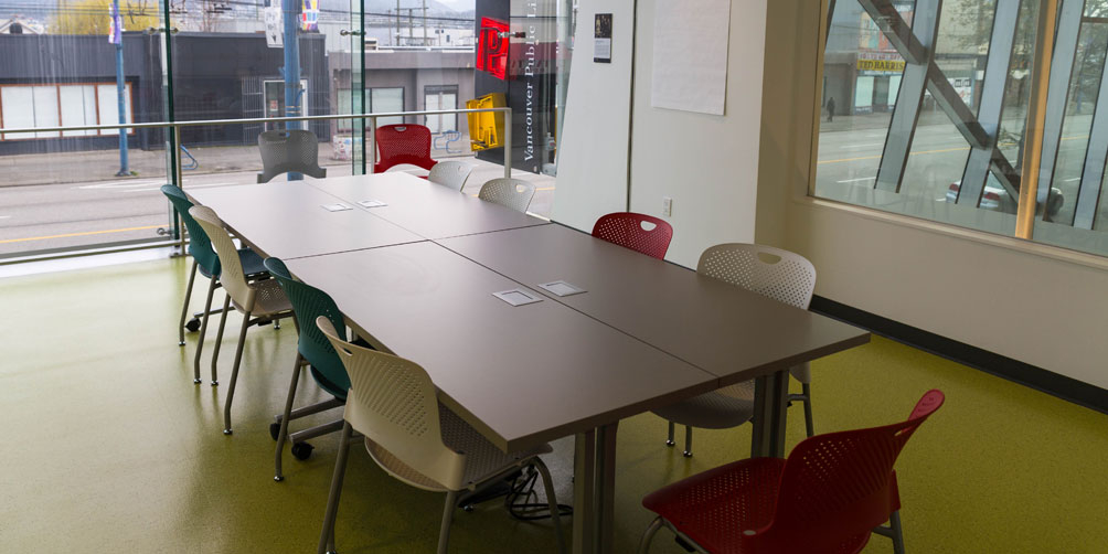 The Nellie Yip Quong Room The Nellie Yip Quong Room, looking toward the back glass wall overlooking the street. There is a large rectangular table made up of four smaller tables pushed together. They are surrounded by eleven chairs.